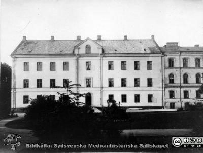 Lasarettsbyggnaden från 1848-50
Från 1868 medicinsk klinik, från 1918 och till 1970-talet lungklinik. Nedersta våningen var från 1918 och till des jubileumskliniken uppfördes på norra området, radiologisk sjukavdelning. Byggnaden var från början reveterad. På Beijers ritning motsvaras den av den västra flygeln. De små vindsgluggarna blev först 1925 ersatta med mansardfönsterkupor. Byggnaden till höger är den 1884 på det äldsta lasarettets (stallmästarehusets) plats uppförda ögonkliniken. Publicerad i Flaum 1968 sid 135. Foto B.A. Lindgren omkr. 1890.
Nyckelord: Kapsel 17;Lund;Lasarett