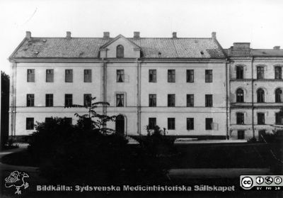 Lasarettsbyggnaden från 1848-50, från 1868 medicinsk klinik, från 1918 lungklinik. Sedan c:a 1970 universitetsinstitution
Nedersta våningen var från 1918 och till dess jubileumskliniken uppfördes på norra området, radiologisk sjukavdelning. Byggnaden var från början reveterad. På Beijers ritning motsvaras den av den västra flygeln. De små vindsgluggarna blev först 1925 ersatta med mansardfönsterkupor. Byggnaden till höger är den 1884 på det äldsta lasarettets (stallmästarehusets) plats uppförda ögonkliniken.- Foto B.A. Lindgren omkr. 1890. Originalfoto, monterat.
Nyckelord: Kapsel 17;Lund;Lasarettet;Lasarett;Södra;Område