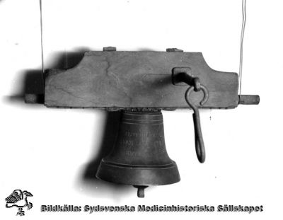 Vällingklocka från Lasarettet i Lund
Omärkt bild. Originalfoto. Monterat. S.k. vällingklocka. Påskrift på klockan: J.P.J Chanzon. Lunds Lazarett. MDCCCLXXX. (dvs 1880).
Klockan användes från början på 1800-talet vid Lunds lasarett för matsignal av spisvärden, en syssla som upphörde 1882 då lasarettet fick ett eget kök. Klockan hängde bl.a. i en alm nära Paradisgatan på södra lasarettsområdet, och ännu 1968 kunde man se märken efter den i trädet (Flaum 1968, sid 122-123). Den finns nu på Kulturen i Lund och kallas där "matklocka" (KM 81820).

Nyckelord: Kapsel 18;Lund;Lasarett;Inventarium