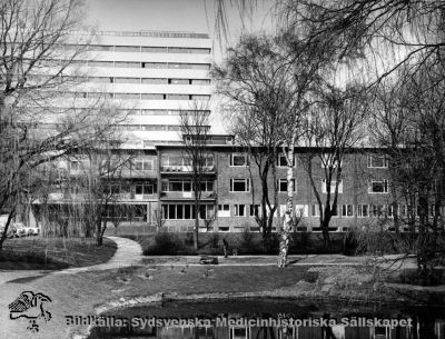 Ögonkliniken i Lund på norra lasarettsområdet, invigd 1942.
Omärkt bild. Originalfoto. Monterat. 
Ögonkliniken i Lund, söderfasaden. Centralblocket (färdigt 1968) i bakgrunden. Foto tidigast 1968, möjligen också på tidigt 1970-tal. Översta balkongen på ögonkliniken blev inbyggd före1975 för att hysa en utvidgad operationsavdelningen, men är på bilden fortfarande inte inbyggd.
Nyckelord: Kapsel 18;Lund;Norra;Område;Fasad