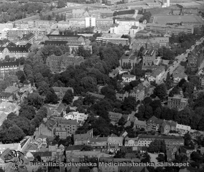 Flygfoto över nordöstra Lund och norra lasarettsområdet i Lund, från sydost. 
I nedre vänstra hörnet ses Akademiska Föreningens tak. Det gamla södra lasarettsområdet skymtar i bildens vänstra kant. I bildens högra del går Sölvegatan upp genom institutionsstaden. På norra lasarettsområdet ser man det nybyggda laboratorieblocket (D-blocket) och till vänster därom AB-blocket med en mycket ljus central del där det blivande centralblocket senare anslöts. Foto i början av 1960-talet.
Nyckelord: Kapsel 18;Lasarett;Lund;Norra;Området;Flygfoto