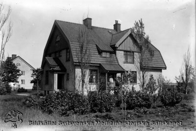 Personalbostäder på St Lars 1929
Påskrift: "S:t Lars museum". Publicerad på sid 113 i Truedsson 1929. Märk mentalskötaren i ljus sommaruniform på husets veranda. Originalfoto senast 1929. Ej monterat
Nyckelord: Kapsel 19;St Lars;Lund;Exteriört