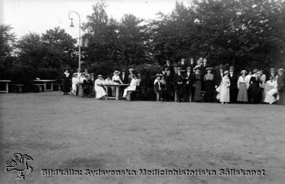 Personal från St Lars samlade i Folkets Park i Lund
Fotografiskt vykort med påskrift på baksidan: "Samling i Folkets park". Vykortet saknar frimärke och poststämpel, och har alltså rimligen aldrig skickats någonstans. Vykort med samma fotografiska teknik har daterats till 1921, och personalens kladsel kan passa med det. Originalfoto. Ej monterat
Nyckelord: Kapsel 20;St Lars;Lund;Personal;Fest;Utflykt;Mentalvårdare;Skötare