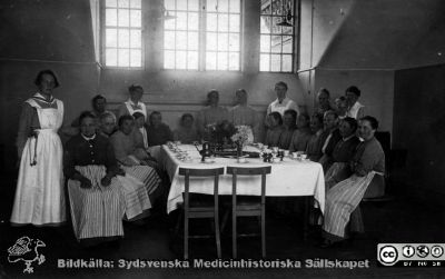 Fest på St Lars "när brödet blev fritt" strax efter första världskriget, 1919?
Kapsel 22 med bilder från St Lars i Lund. Påskrift: "Fest. 'När brödet blev fritt', asylens arbetssal 1919?" Vykort, adressat: "Fru Ruth Lindbäck, Fogdarp". Korrespondens: "Jag gick och väntade på dig när du var i staden men inte kom du. Jag är så nyfiken på kortet ni tog, blev det bra. Detta här är att som vi tog när brödet blev fritt vi har ej så många patienter med, men dom som är med har blivit bra, i synnerhet  dem gormiga Bothildan henne känner du nog igen. Skrif en gång. Agnes". Originalfoto. Ej monterat
Nyckelord: Kapsel 22;St Lars;Lund;Patienter;Personal;Ransonering;Fest