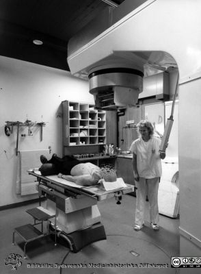 Onkologiska kliniken i Lund. Accelerator ("strålkanon") på högvoltsavdelningen. 
Foto Ola Terje låda A bild 14/7. Slutet på 1980-talet. Assistenten hette troligen Inger.
Nyckelord: Onkologiska kliniken i Lund. Högvoltsavdelningen. Accelerator. 