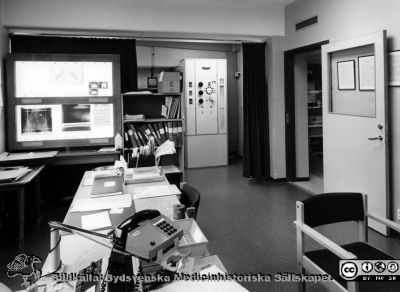 Onkologiska kliniken i Lund. Förrum till applikationssal för gynekologisk onkologi. 
Foto Ola Terje låda A bild 37/9. Slutet på 1980-talet.  I bakgrunden ett ljusskåp med bäckenröntgenbild och ett skåp märkt "Cathetron", en apparat för efterladdning av radioaktiva preparat.
Nyckelord: Terje;Onkologisk;Onkologi;Klinik;Lund;Interiör;1980-talet;Förberedelserum;Gynekologi;Ljusskåp