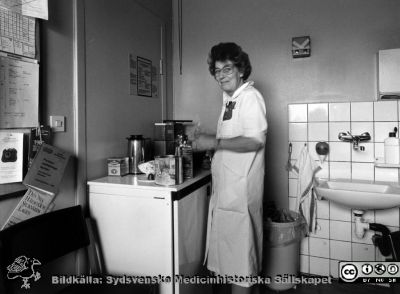 Onkologiska kliniken i Lund. Kaffe lagas.
Foto Ola Terje låda A bild 47/12. Slutet på 1980-talet. Städerskan "Kaffe-Margit", klinikens allt-i-allo.
Nyckelord: Terje;Onkologisk;Onkologi;Klinik;Lund;Interiör;1980-talet;Pausrum;Kaffekokning