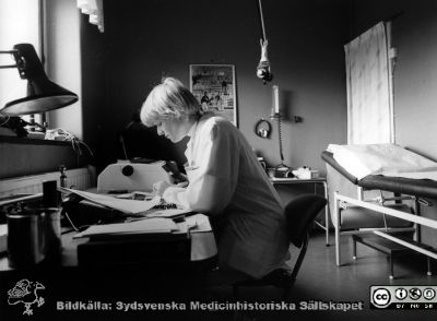 Onkologiska kliniken i Lund. Dr Eva Bruhn dikterar journalanteckning på ett undersökningsrum
Foto Ola Terje låda A bild 50/9. Slutet på 1980-talet. 
Nyckelord: Terje;Onkologisk;Onkologi;Klinik;Lund;Interiör;1980-talet;Undersökningsrum