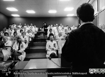 Radiologiska / onkologiska kliniken i slutet av 1980-talet
Foto Ola Terje låda B. 63/11. Föreläsningssalen. 1:a raden från vänster, sjukhusfysiker Ulla-Britta Nordberg, dr Ilva Bostedt, dr Per Malmström, sjuksköterska Rut Kristenssen (halvt ansikte) 2:a raden från vänster, ? (halvt ansikte), ?, ?, avdelningsföreståndare Karin Robertz, ? vårdlärare Margit Persson (halvt ansikte), 3:dje raden från vänster, dr Lars Brandt, dr Bengt Kallum, undersköterska Evy Andersson, sjuksköterska Rauni Maraste, dr Asma Mohamed el Hassan, sjukskötare Stefan Johnsson, avdelningsföreståndare Monica Emmertz, undersköterska Margit Ahl (halvt ansikte) 4:de raden från vänster, okänd, radioterapiassistent AnnMargret Engström, avdelningsföreståndare Eva Englund, dr  Sven-Börje Ewers, radioterapiassistent Tomas Jansson, okänd, okänd, radioterapiassistent Lena Andreasson, undersköterska Petra Hermansson. 5:te raden från vänster, okänd, okänd, sjuksköterska Helena Winqvist, undersköterska Siv Andersson, 3 okända, undersköterska  Irene Magnusson, okänd, skötare Greta Isaksson. Översta raden från vänster, sjukhusfysiker Andrzej Tomaszewicz, okänd, dr Sten Graffman, dataoperatör Ronny Jansson, okänd,okänd, lab-ass Ghita Fallenius, lab-ass Ann Brun. Föreläsare okänd. Originalfoto. Ej monterat
Nyckelord: Lasarettet;Lund;Universitet;Universitetssjukhus;USiL;Radiologi;Onkologi;Föreläsning;Utbildning