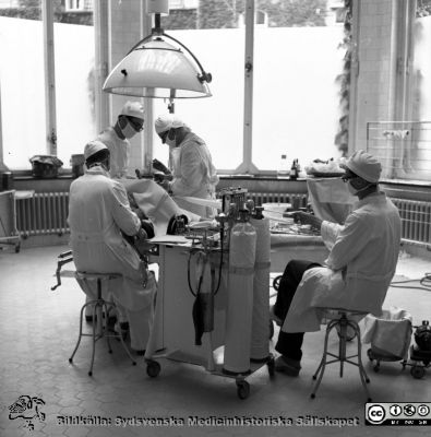 Prof Helge B Wulff opererar på kirurgiska kliniken i Malmö. 
Dr. Olle Lundskog söver. En kandidat sitter på en stol och drar i ett band till en sårhake. Album äldre neg. 1951-1958 MAS, från fotograf Björn Henrikssons samling. Negativ
Nyckelord: Malmö;MAS;Kirurgi;Operation;1950-talet