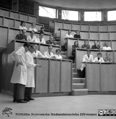 Malmö Allmänna Sjukhus. Nya aulan, första föreläsningen, 6/4, 54. 
Pärm äldre neg. 1951-1958 MAS, från fotograf Björn Henrikssons samling. Professor Helge B. Wulff med doc. Knut Haeger bakom sin rygg. Från negativ
Nyckelord: Aula;MAS;UMAS;Malmö;Allmänna;Sjukhus;Utbildning;Föreläsning