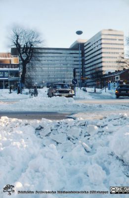 Centralblocket på Lasarettet i Lund en vinter under något av 1900-talets sista decennier, före 1986. 
Helikopterplattan på sjukhusets tak är ännu inte byggd och inte heller glaspartiet vid huvudentrén (byggt 1986).
Nyckelord: Lasarett;Lund;Universitet;Universitetssjukhus;Exteriör;Fasad;Vinter