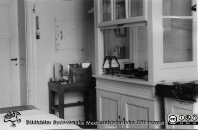 Packningsrum för radiuminläggningar på radiologiska kliniken, 1930-talet
Tjänstgjorde också som behandlingsrum. Radiologiska kliniken 1939. Skåpet på bortre väggen var radiumförrådet. 
Från Thyra Åhlunds och Astrid Bjelks fotosamling skänkt till Radiologiska kliniken 10/4 1982. Thyra Åkhlund (1907-1988) var sjuksköterska på radiologiska kliniken 1931-1942 och Astrid Bjelk från 1933 till sin pensionering.
Nyckelord: Laboratorium;Lasarettet;Lund;Universitetssjukhuset;USiL;Radiologisk;Röntgenologisk;Onkologisk;Klinik;Radium