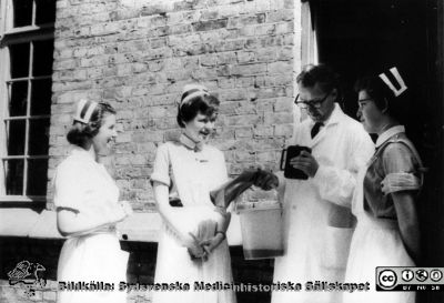 Personal på urologiska kliniken i Lund i mitten på 1900-talet
Urologisk avdelning urologi låda A 3:2
Vid entrén till urologiska kliniken i gamla kirurgibyggnaden i Lund. Längst till vänster Syster Maj-Britt Jönsson. Underläkaren är Lennart Andersson, senare professor i urologi i först Umeå och senare i Stockholm. Han är just på väg till Koagulationslaboratoriet i Malmö med ett urinprov i spannen, för analys av fibrinolyshämmaren epsilonaminokapronsyra. I vänster hand har han troligen en bandspelare-diktafon, Sony. Foto på 1950-1960-talen.
Nyckelord: Lasarettet;Lund;Universitetssjukhuset;Urologisk;USiL;Kirurgisk;Klinik;Kapsel 11