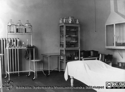 Ett undersökningsrum och laboratorium på ögonkliniken i Lund i mitten på 1920-talet. 
Professorn, Gustaf Ahlström, gjorde själv bakterieodlingar och mikroskopiska undersökningar, och inredningen med ett dragskåp och utrustningen i bakgrunden talar för att detta är den lokal där prover togs och bearbetades.
