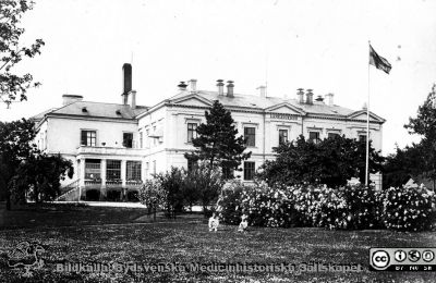 Länssjukhuset i Ystad
Länssjukhuset i Ystad. Fasad mot söder. Foto på ortokromatisk film, d v s före mitten på 1920-talet efetersom svenska flaggan sys med mörkt kors på ljus botten. Bildkälla Denise Andersson 2021. Ur  hennes mans farfars efterlämnade bilder. Denne var Charly Urbanus Andersson, 18920525-3918, född i Ljunits, Sjörups församling vid Ystad, död 1974-02-14 och då kyrkobokförd på S Vallösa 5, 27012 Rydsgård. Han var skräddare och fotograf, bosatt i Vallösa utanför Ystad. Fotografens mor skall ha tillbringat sina sista år här som mycket gammal.
Nyckelord: Skräddare;Fotograf;Länslasarett;Huvudbyggnad.