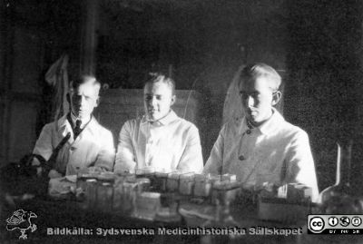Bilder från histologiska avdelningen på anatomiska institutionen i Lund år 1923
Fotoalbum märkt 1923 på första bladet. Det innehåller bilder från dåvarande histologiska avdelningen 
på anatomiska institutionen i Lund på Biskopsgatan 7. Bildtext: Erik Larsson. Joel Jönsson, Folke Bohman.  
De  förefaller sitta i i histologens kurslaboratorium för att tillverka histologiska preparat. Arbetsbordet är fyllt med små glasvannor för preparatfärgning. 
Bildkälla Stiftelsen Locus Medicus Lundensis 250317. Fotograf okänd.
Nyckelord: Histologiska avdelningen;Anatomiska Institutionen;Locus Medicus Lundensis;Stiftelse;Medicinska fakulteten i Lund;Lunds universitet;Medicine studerande;Studenter;Kurslaboratorium