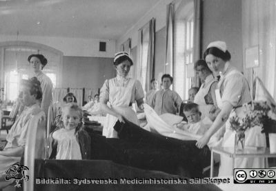 Interiör från en stor vårdsal med blandad beläggning med barn och kvinnor. 
Bild 24 i husmor Anna Landelius (1880-1964) efterlämnade fotoalbum. Ingrid Frennhoff (f. 1944) hade övertagit detta album efter sin morfar som i sin tur tagit hand om det efter sin syster husmor Anna på Lasarettet i Lund. Gåva till Sydsvenska Medicinhistoriska Sällskapet nyåret 2020.- Skulle kunna vara en av 20-bäddssalarna på Malmö Allmänna Sjukhus. Sköterskeeleven längst till höger är möjligen Anna Landelius.
Nyckelord: Sjukhussal;Sjuksal;Malmö Allmänna Sjukhus;Vårdsal;Barn;Blandad;MAS