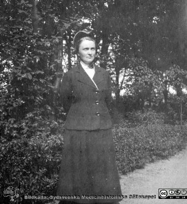 Sjuksköterska i vinteruniform. 
Bild 68 i husmor Anna Landelius (1880-1964) efterlämnade fotoalbum. Ingrid Frennhoff (f. 1944) hade övertagit detta album efter sin morfar som i sin tur tagit hand om det efter sin syster husmor Anna på Lasarettet i Lund. Detta album är en gåva från Ingrid Frennhoff till Sydsvenska Medicinhistoriska Sällskapet nyåret 2020.

Kan vara en SSSH-sköterska, men knappast Anna Landelius. Foto i en park.
Nyckelord: Sjuksköterska;Vinteruniform