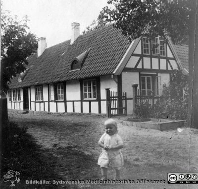 Litet barn vid lantgård. 
Bild 80 i husmor Anna Landelius (1880-1964) efterlämnade fotoalbum. Ingrid Frennhoff (f. 1944) hade övertagit detta album efter sin morfar som i sin tur tagit hand om det efter sin syster husmor Anna på Lasarettet i Lund. Detta album är en gåva från Ingrid Frennhoff till Sydsvenska Medicinhistoriska Sällskapet nyåret 2020.
Kanske Anna Landelius fädernegård Jakobslund i Ljungsbro?
Nyckelord: Spädbarn;Lantgård