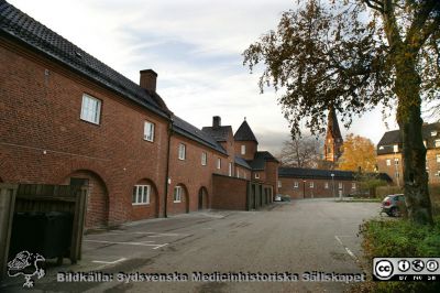 Universitetssjukhuset i Lund. Till vänster och i fonden den ovanjordiska förbindelsegången mellan södra och norra lasarettsområdet, byggd 1918 (byggnad 24). 
Till vänster och i fonden den ovanjordiska förbindelsegången mellan södra och norra lasarettsområdet, byggd 1918 (byggnad 24). Nu finns Livets Museum i den sedan 2012.  Foto mot väster. Gamla kvinnokliniken (nu Rehabhuset) till höger. Allhelgonakyrkans torn i bakgrunden. Foto B. Ehinger.
Nyckelord: Kulvert;Ovanjordisk;Förbindelsegång;Lasarett;Lund;USiL;Kvinnoklinik;Gynekologisk;KK