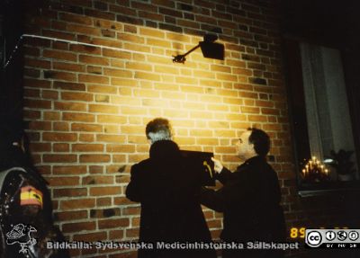 Ortopediska kliniken i Lund11989.  Docent Göran Sundén (?)  och docent Lars Lidgren hjälps åt att sätta upp en minnestavla.
Från ortoped klin album 01, Lund. Fotograf Berit Jakobsson. 1989. En minnesplakett sätts upp på dåvarande ortopediska klinikens hus för att påminna om klinikens 75-årsjubileum. Huset tillkom 1929. Docent Göran Sundén (?) och docent Lars Lidgren hjälps åt.
Nyckelord: Lund;Universitetssjukhus;USiL;Kliniker;Ortopedi;Läkare;Ledproteser;Minnesmärken