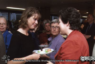 Ortopediska kliniken i Lund 2000.Vårdadministratören Berit Jakobsson avtackas i sjukhusaulan.
Från ortoped klin album 01, Lund. Fotograf Berit Jakobsson. 2001. Mingel utanför sjukhusets aula. Sjuksköterskan Helene Eriksson, sjukgymnasten Eva Nordell och sjuksköterkan Agneta Theren i samkväm i sjukkhusaulans nedre foajé i samband med framförandet av  Henning Mankells monolog "Grävskopan" med Tommy Borgström från Ystads Stående Teatersällskap, specialskriven för honom. Föreställningen gavs  inför klinikens personal som avtackningspresent till klinikföreståndaren och vårdadministratören Berit Jakobsson.
Nyckelord: Lund;Universitetssjukhus;USiL;Kliniker;Ortopedi;Personal;Personalträff