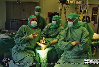 Ortopediska kliniken i Lund  2001. Ortopeder inför en operation på en fot. 
Från ortoped klin album 01, Lund. Fotograf Berit Jakobsson. 2001. Ortopeder inför en operation på en fot. Det är fritt fram att gissa vad de egentligen har för sig. Den intensiva ögonkontakten mellan kirurg och operationssköterska betyder kanske att en flört pågår? De övriga förefaller svalt avvaktande.
Nyckelord: Lund;Universitetssjukhus;USiL;Kliniker;Ortopedi;Operationsavdelning;Läkare