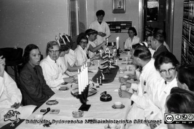 Luciafest på radiologiska kliniken i Lund, troligen på 1950-talet. 
Sjuksköterskor, sekreterare och läkare runt bordet. Institutionssekreterare Gun Björk  sitter som nr 2 från vänster. Vid sidan om henne sitter Gunhild Åkerman, sjuksköterska. Klinikchefen docent Bertil Ebenius sitter på bordets högra sida som nr 3 från kameran. Bortom honom sitter troligen Martin Lindgren i grå kavaj. Foto troligen på 1950-talet. Från Syster Elinas fotoalbum (Elina Holmberg?).
Nyckelord: Radiologisk;Onkologisk;Klinik;Lasarettet i Lun;Lussekaffe