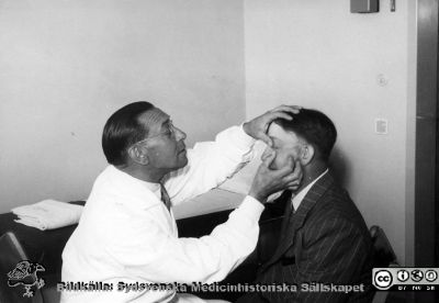 Docent Bertil Ebenius (1902-1959) undersöker en patient på radiologiska kliniken i Lund. 
Foto på 1950-talet. Från Syster Elinas fotoalbum (Elina Holmberg?) .
Nyckelord: Radiologi;Onkologi;Jubileumsklinik;Lasarettet i Lund