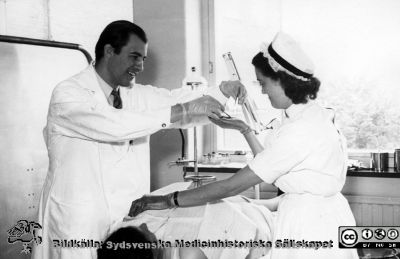 Okänd läkare i arbete med att ta en ytlig biopsi på radiologiska kliniken i Lund tillsammans med en sofiasyster. 
Från Syster Elinas fotoalbum (Elina Holmberg?).
Nyckelord: Radiologisk;Onkologisk;Jubileumsklinik;Lasarettet i Lund;Poliklinik;Provtagning