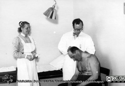 SSSH-sjuksköterska och en läkare undersöker en patient på radiologiska kliniken i Lund,
Foto troligen på 1950-talet. Från Syster Elinas fotoalbum (Elina Holmberg?).
Nyckelord: Radiologisk;Onkologisk;Jubileumsklinik;Patient;Undersökning