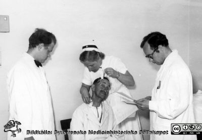 Två läkare och en SSSH-sjuksköterska undersöker och behandlar en patient på radiologiska kliniken i Lund. 
Troligen på 1950-talet. Från Syster Elinas fotoalbum (Elina Holmberg?).
Nyckelord: Onkologisk;Radiologisk;Jubileumsklinik;Lasarettet i Lund