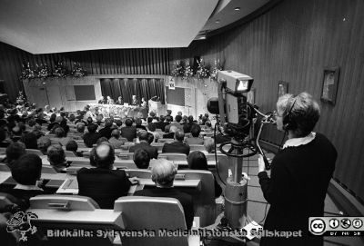 Forskningens Dag 1983 i Lund
Lasarettsfotograferna i Lund,  pärm  Sv/v Neg, 83:2. Forskningens Dag 1983 i Lund: "Cancerforskning - en nyckel til liv". Översiktsbild av den fullsatta aulan på Lasarettet i Lund. Sveriges kungapar, Drottning Siliva och kung Carl XVI Gustaf sitter främst i publiken. Evenemanget filmades och sändes till angränsande salar och på sjukhusets intern-TV. Från foto.
Nyckelord: Lasarettet;Lund;Universitetssjukhuset;USiL;Forskningens Dag;Cancer