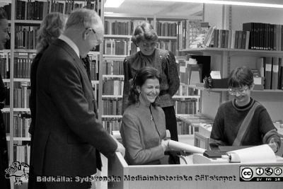 Drottning Silvia låter sig roas på sjukhusbiblioteket i Lund 1983
Lasarettsfotograferna i Lund,  pärm  Sv/v Neg, 83:2. A. 83-11-10. Forskningens Dag 1983. Drottning Silvia har roligt när  bibliotekarien på sjukhusbiblioteket demonstrerar något på fjärrskrivmaskinen. Hon hittade kanske något trevligt i det då alldeles nya datoriserade söksystemet för litteratu. Chefläkaren professor Hans Rorsman står bredvid tillsammans med annan personal eller hovdamer. Från negativ
Nyckelord: Lasarettet;Lund;Universitetssjukhuset;USiL;Silvia;Drottning;Sjukhusbiblioteket