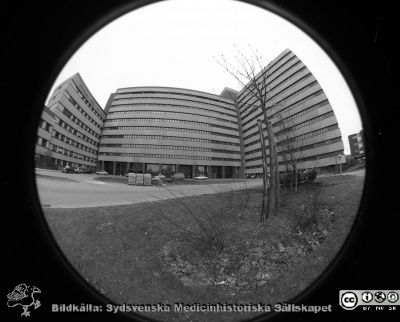 Centralblocket i Lund med nytt objektiv
Lasarettsfotograferna i Lund,  pärm  Sv/v Negativ, 1985. 31/85. Centralblocket på Lasarettet i Lund provfotograferat med fotoavdelningens nya fina supervidvikelobjekti, typ "Fisheye". Vy av byggnadens fasad mot väster med huvudentrén. Till vänster AB-blocket, till höger onkologiska kliniken och kvinnokliniken. Från negativ
Nyckelord: Lasarettet;Lund;Universitetssjukhuset;USiL;Centralblocket;Entr