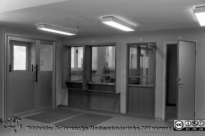 Akutmottagningen i Lund före ombyggnad 1985
Lasarettsfotograferna i Lund,  pärm  Sv/v Negativ, 1985. 85/58. Patientsidan på expeditionsluckorna på akutmottagningen före ombyggnad. Patienterna kom in genom dörren till vänster. Från negativ
Nyckelord: Lasarettet;Lund;Universitetssjukhuset;USiL;Akutmottagning;Entr;Ombyggnad