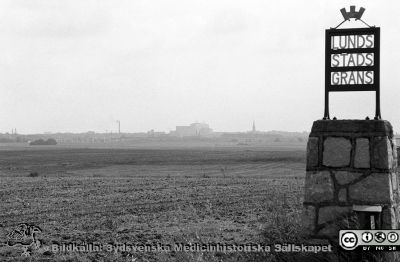 Lunds stadsgräns i väster
Lasarettsfotograferna i Lund,  pärm  Sv/v Negativ, 1985. 85/62. Lunds stadsgräns från väster. Centralblocket och Allhelgonakyrkan skymtar i horisontens dis, liksom fjärrvärmeverkets höga skorsten. Från negativ
Nyckelord: Lasarettet;Lund;Universitetssjukhuset;USiL;Stadsgräns;Skylt