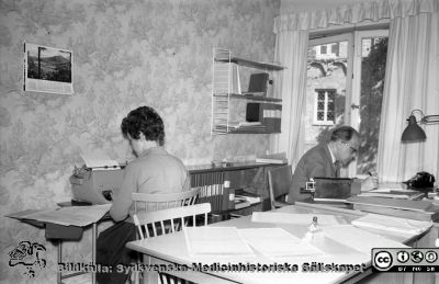 Gamla sjukhuskontoret vid Allhelgona Kyrkogata
Lasarettsfotograferna i Lund,  pärm,  96+97 (?).14. Gamla kontoret. Från negativ. Troligast reprofoto av bild SMHS280 från sjukhuskontoret vid Valvet på södra lasarettsområdet. Kanske Per-Börje Jönsson vid skrivbordet. Bokhyllan på väggen är en s.k. String-hylla, populär på 1950-talet. Räknesnurran är handvevad, och skrivmaskinen är nog av mekanisk typ. Foto 1960, kanske inför avflytten till norra lasarettsområdet c:a 1960.
Nyckelord: Lasarettet;Lund;Universitetssjukhuset;USiL;Administration;Kontor