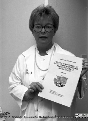 Sjuksköterskan Marie Holmberg med slutrapporten till en historiskt viktig utredning
Lasarettsfotograferna i Lund.  Blandade negativ, omärkta år 1988-1995 (lösa negativhållare). Omärkt bild. Cancerfondens vårdkvalitetskprojet "Personlig kontinuerlig kontakt för kvinnor med nydiagnosticerad bröstcancer" visas upp, publicerad 1992 av Marie Holmberg och Christian Ingvar. Från negativ.
Nyckelord: Lasarettet;Lund;Universitetssjukhuset;USiL;Forskning;Cancer;Onkologi;Omvårdnad