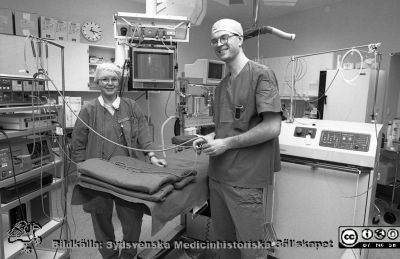 Urologen docent Ola Bratt i en operationssal för urologi 1995
Lasarettsfotograferna i Lund.  Blandade negativ, omärkta år 1988-1995 (lösa negativhållare). Foto för Stig Mårtensson för urologiska klinikens årsredovisning. 95-04. Urologen docent Ola Bratt i en operationssal för urologi tillsammans med operationssköterskan Kerstin Virdefors, chef för de urologiska operationssköterskorna. De står framför klinikens färgämneslaser som användes för att skjuta sönder uretärstenar. Från negativ.
Nyckelord: Lasarettet;Lund;Universitetssjukhuset;USiL;Urologisk;Klinik;OperationsAvdelning