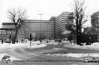 Centralblocket på Lasarettet i Lund en vintrig dag i slutet på 1980-talet, senast 1988. 
Foto från huvudentrén vid Getingevägen. 1960-talets administrationsbyggnad till vänster, ännu ej med tillbyggnaden för patienthotellet. Dess födrsta etapp kom c:a 1988. Portvaktshuset närmast kameran till höger och centraltandpolikliniken längre bort. Satellitantennerna sitter kvar på centralblockets tak. De togs ned i mitten på 1990-talet.
Nyckelord: Lasarettet;Lund;Universitetssjukhuset;USiL;Centralblocket;Centraltandpolikliniken;Administration;Portvakt