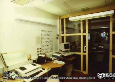 Modellprojektet "Vårdavdelning 2000"
Sekrerarrum med diktafon och elektrisk skrivmaskin. En dator står i bortre hörnet och ger inte intryck av att vara tänkt som ett särskilt viktigt arbetsredskap. 
"Vårdavdelning 2000" var en modellavdelning inför 2000-talets renoveringar av avdelningar i Blocket i Lund, utformad 1988 - 1990 under ledning av Elwy Ekman. Från originalfoto. Foto 1988-1990. 
Nyckelord: Lasarettet;Lund;Universitetssjukhuset;USiL;Vårdavdelning 2000;Sekreterarrum