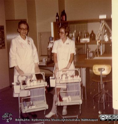 Laboratoriesjuksköterskan Ingar Widner och en sköterska eller biträde med rondvagnar. 
Karl Emil Thulins efterlämnade fotoalbum. 1970-talet, i infektionsklinikens bibliotek. Omärkt bild. Från originalfoto.
Nyckelord: Lasarettet;Lund;Universitetssjukhuset;USiL;Epidemi;infektion;Kliniken