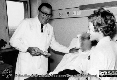 Professor Gösta Jönsson går avskedsrond och har just fått en bok i present aven patient i sängen. 
Urologen avd. 21, 1975. Längst till höger avdelningsföreståndaren Eva Ljunggren. Bildkälla Eva Ljunggren 2016.
Nyckelord: Lasarettet;Lund;Urologiska;USiL;Universitetssjukhuset;Kliniken