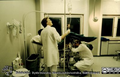 Urologiska klinikens mottagning i mitten på 1970-talet.
Album Urologiska kliniken i Lund 20 år 1977-10-01. Omärkt diabild. Sjuksköterskan Marianne Nilsson assisterar vid en typisk cystoskopisituation. Den undersökande läkaren är inte identifierbar. Urologiska kliniken i Lund, mottagning 7. Bildkälla Bengt Uvelius.
Nyckelord: Lasarettet;Lund;Universitetssjukhuset;USiL;Urologiska;Kliniken;Mottagning