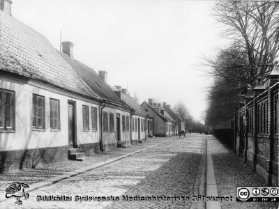 Norra Vallgatan i Lund före 1918, österut
Omärkt bild. Originalfoto, monterat
Med hög sannolikhet Norra Vallgatan i Lund innan fastigheterna på gatans norra sida (till vänster i bild) inkorporerades i södra lasarettsområdet och revs för att ge plats för 1918 års röntgeninstitut, kirurgisk poliklinik, 1929 års köksbyggnad mm. Vy österut. Norra gaveln på Thomanderska studenthemmet anas i gatans högerkant vid dess slut. Rakt fram fortsätter gatan in i nuvarande Biskopsgatan. Till höger i bilden ses det gamla södra lasarettsområdets mur mot norr. Delar av den finns kvar ännu 2016.
Nyckelord: Kapsel 17;Lund;Lasarettet;Lasarett;Söder;Södra