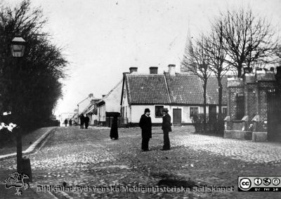 Östra delen av Norra Vallgatan i Lund under något av decennierna runt sekelskiftet 1900
Omärkt bild. Originalfoto, monterat
Norra Vallgatan i Lund innan fastigheterna på gatans norra sida (till höger i bild) inkorporerades i södra lasarettsområdet och revs för att ge plats för 1918 års byggnad med röntgeninstitut, kirurgisk poliklinik, 1929 års köksbyggnad mm. Vy västerut från korsningen med Sandhatan. Allhelgonakyrkans torn i bakgrunden. Biskopshusets staket till höger i bild.
Nyckelord: Kapsel 17;Lund;Lasarettet;Lasarett;Södra;Område