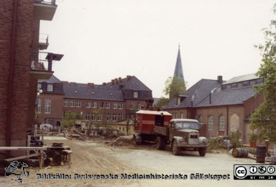 Markarbeten för öronklinikens annex
Kapsel 26. Vy mot söder med dåvarande medicinska kliniken i fonden. Öronklinikens huvudbyggnad ses till vänster och 1918 års panncentral till höger, verkstäder när  fotot togs, riven 2011. Omonterad Agfa färgpapperskopia stämplad 698A 27.6.6X. Inga andra identifierande påskrifter. I mapp från sjukhusdirektörens arkiv med påskrift "Div. färgfoto + kartor". Foto troligen på 1950-talet.
Nyckelord: Kapsel 26;Lasarettet;Lund;Bygge;ron;Klinik