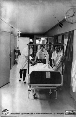 Transport av patient i säng med droppställning
Brun ringbunden mjuk pärm, kirurgiska kliniken i Lund. Andningsstöd ges med Rubens blåsa. Foto
